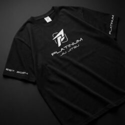 Black Platinum Jiu Jitsu t-shirt flat lay on dark background, white logo on chest, EST 2024 text on sleeve, premium BJJ lifestyle apparel.